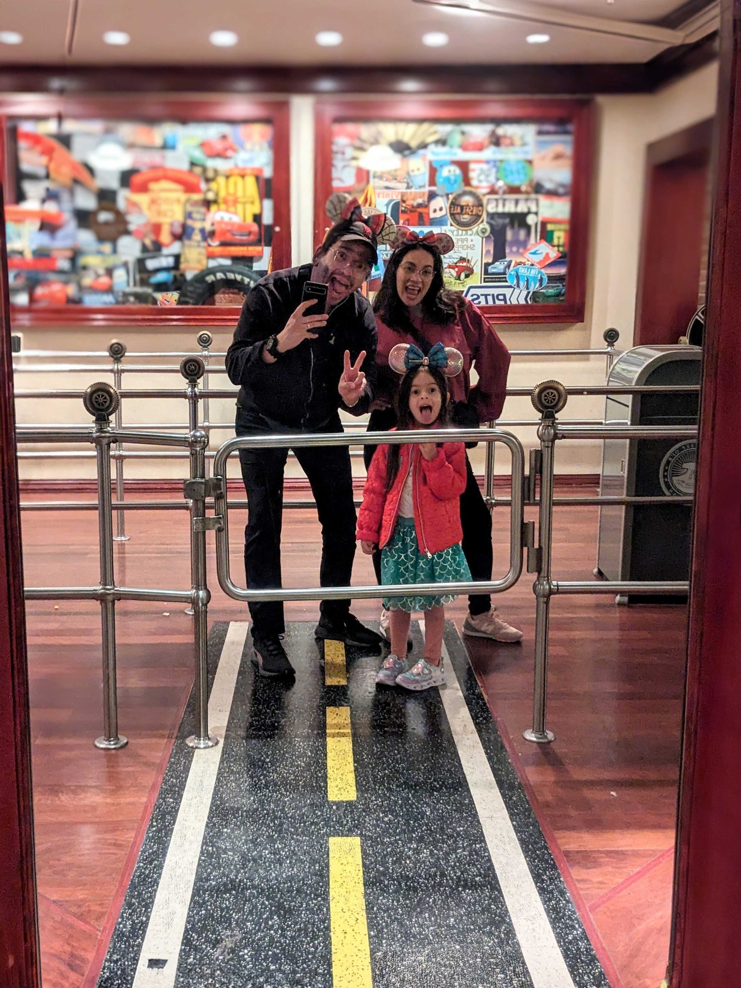 mom dad and daughter wearing mickey mouse ears posing infront of a mirror inside luigis casa della tires at Disneys CA adventure